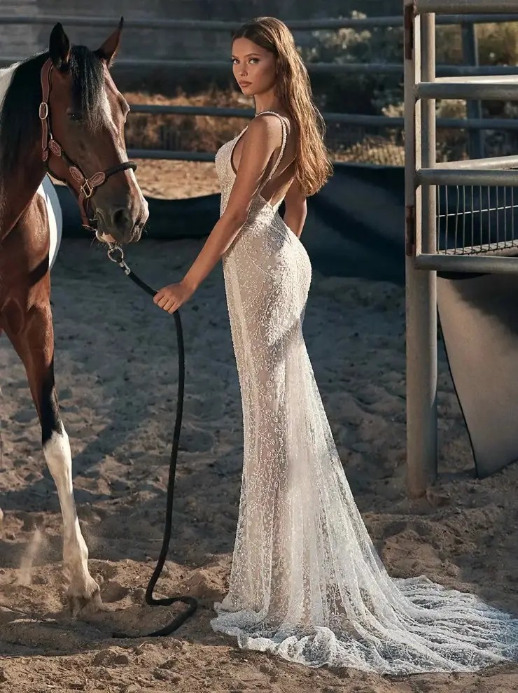 Model is wearing a fit and flare spaghetti strap wedding dress with a plunging neckline 