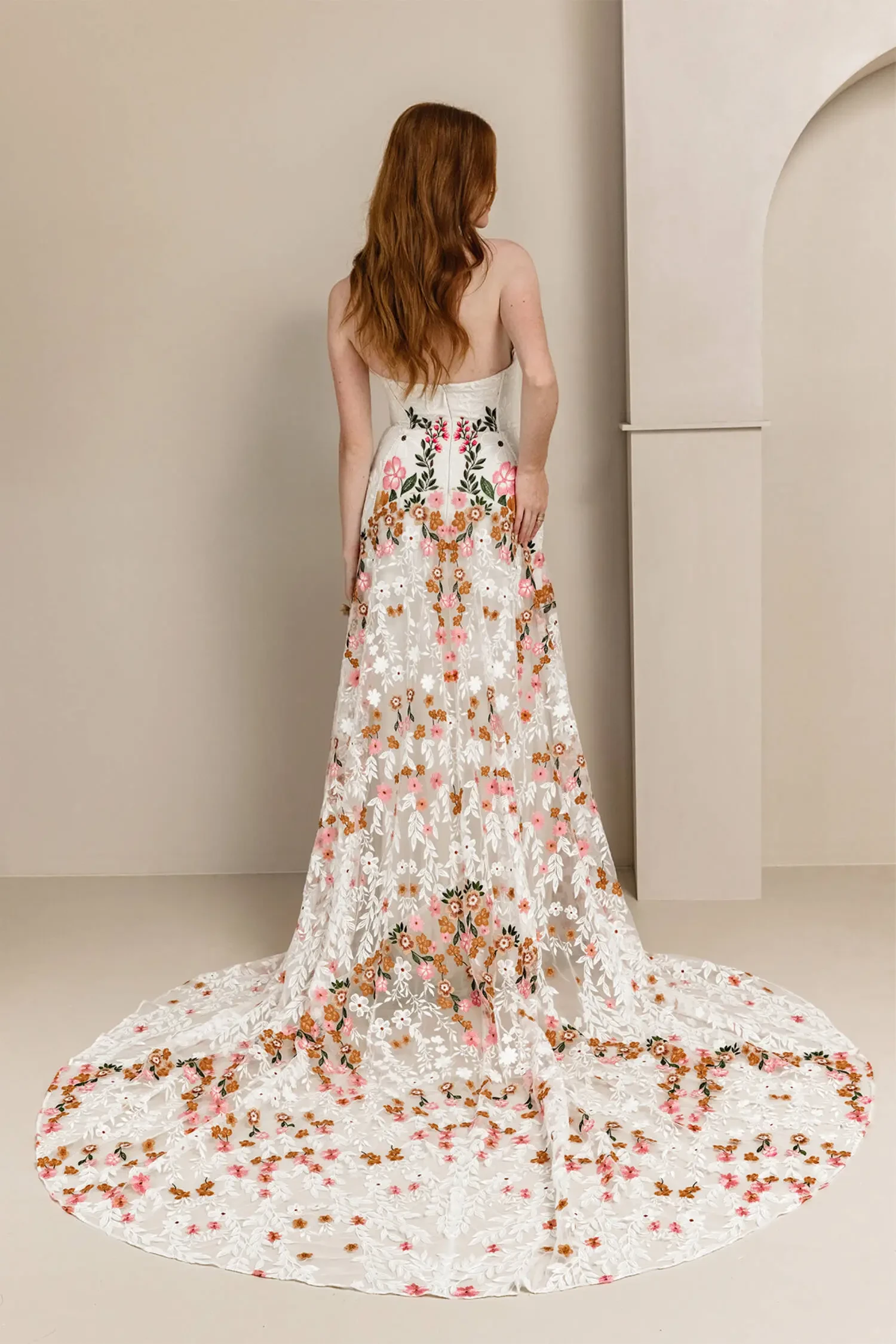 Model is wearing a sand-dyed tulle wedding gown with vibrant floral embroidery, a fully boned bodice, and a dramatic embroidered train.