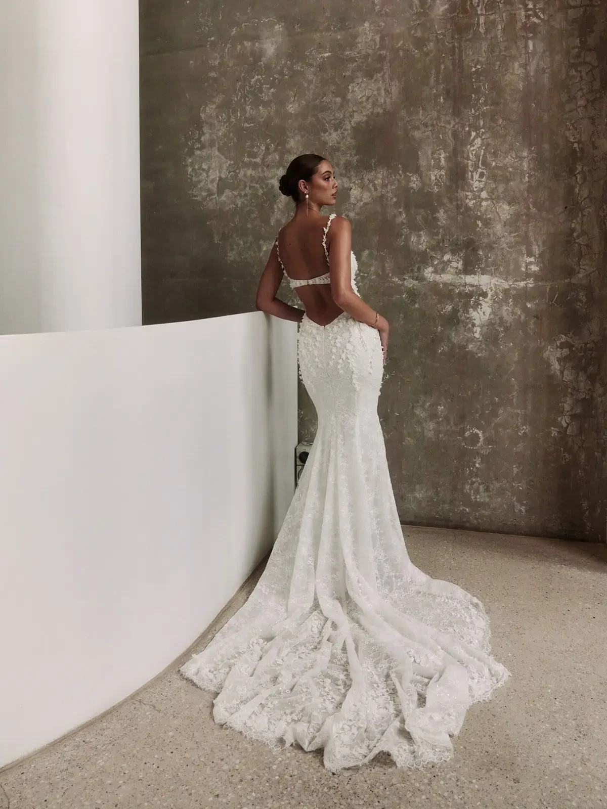 Model is wearing a romantic open-back gown with cascading 3D floral appliqués, a deep scoop back, and a soft, flowing silhouette.