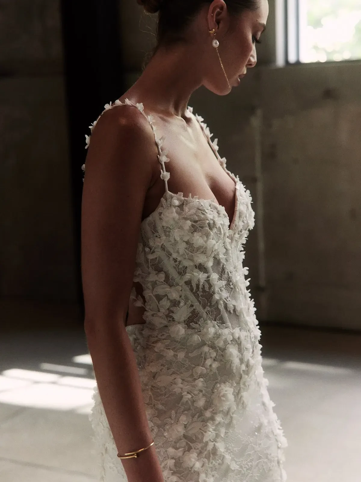 Model is wearing a romantic open-back gown with cascading 3D floral appliqués, a deep scoop back, and a soft, flowing silhouette.