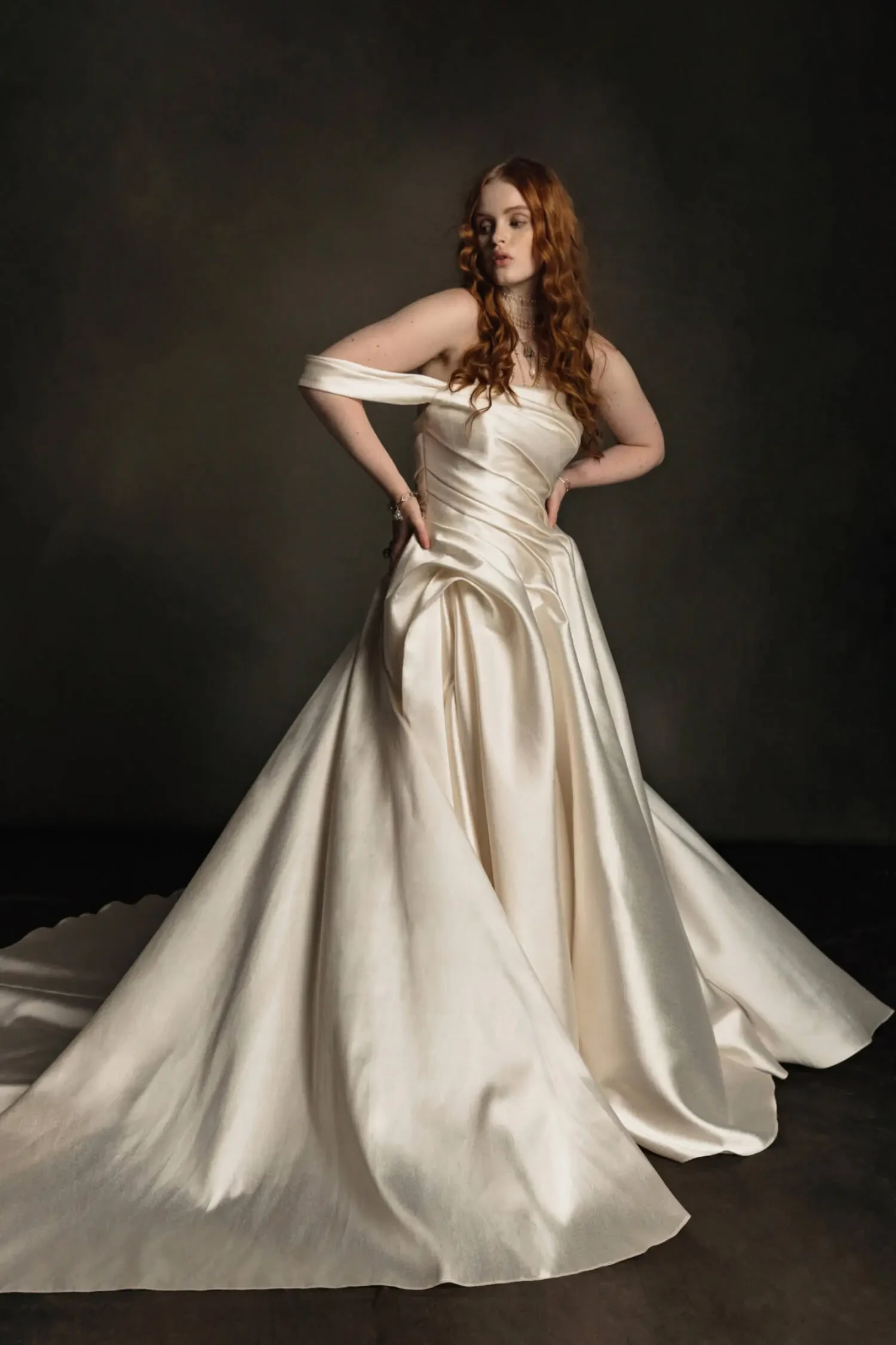 Model is wearing a mikado gown with an asymmetrical draped shoulder, structured bodice, voluminous skirt, and dramatic folded train.