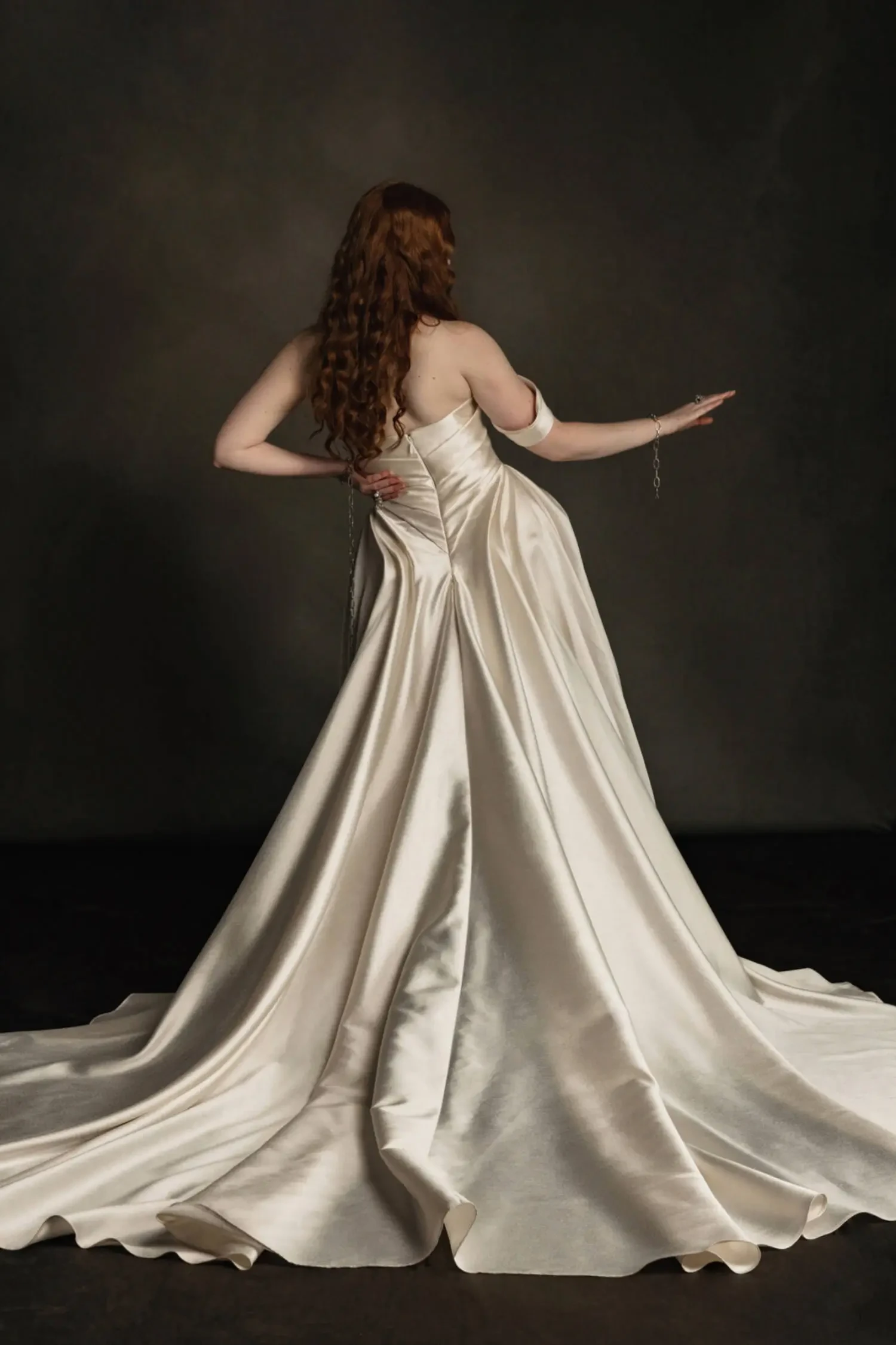 Model is wearing a mikado gown with an asymmetrical draped shoulder, structured bodice, voluminous skirt, and dramatic folded train.