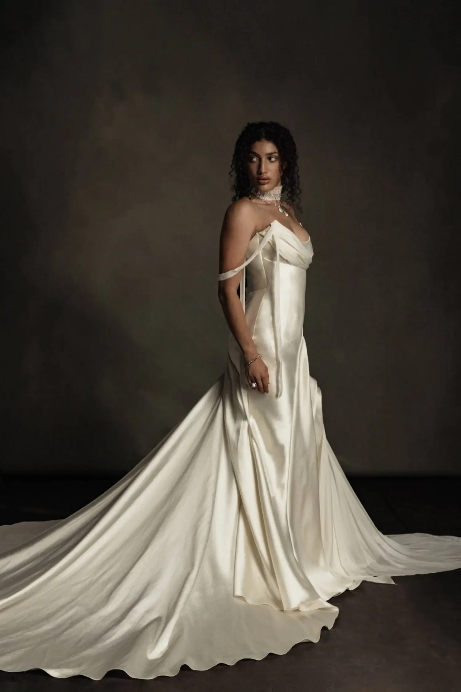 Model is wearing a gown with a structured bodice, flowing boiled chiffon inserts, body-contouring pleats, and a long sweeping train.