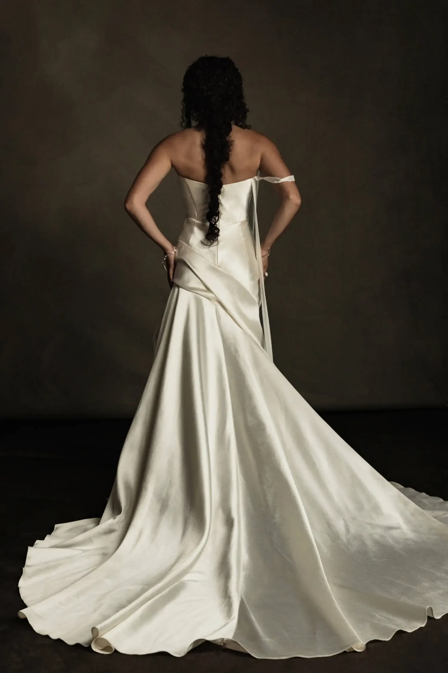 Model is wearing a gown with a structured bodice, flowing boiled chiffon inserts, body-contouring pleats, and a long sweeping train.