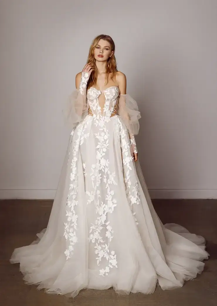 A model wearing an elegant wedding gown with a fitted bodice, off-the-shoulder sleeves, and floral lace detailing, posing against a neutral background.