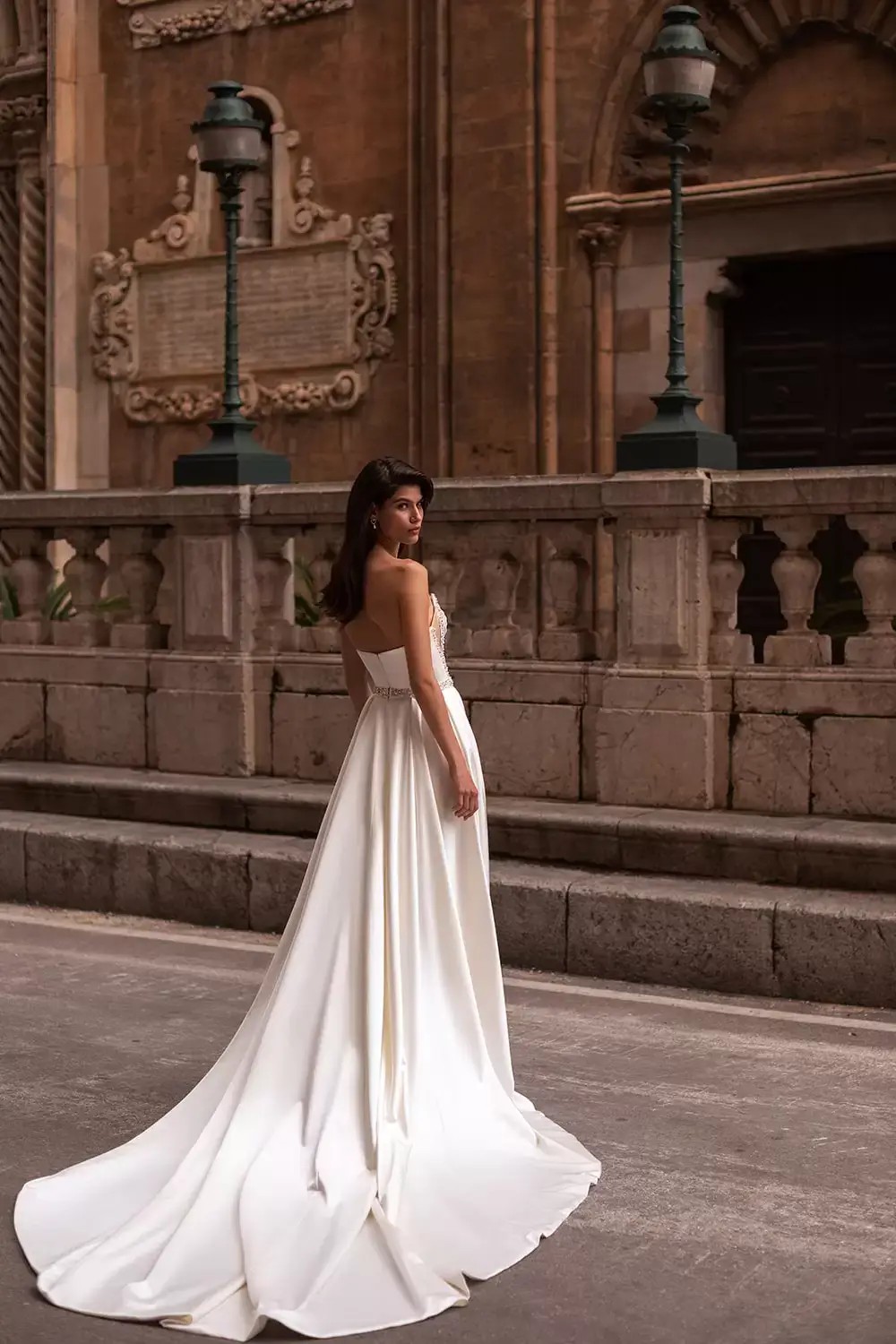 Model is wearing a strapless satin wedding dress with crystal accents by eva lendel