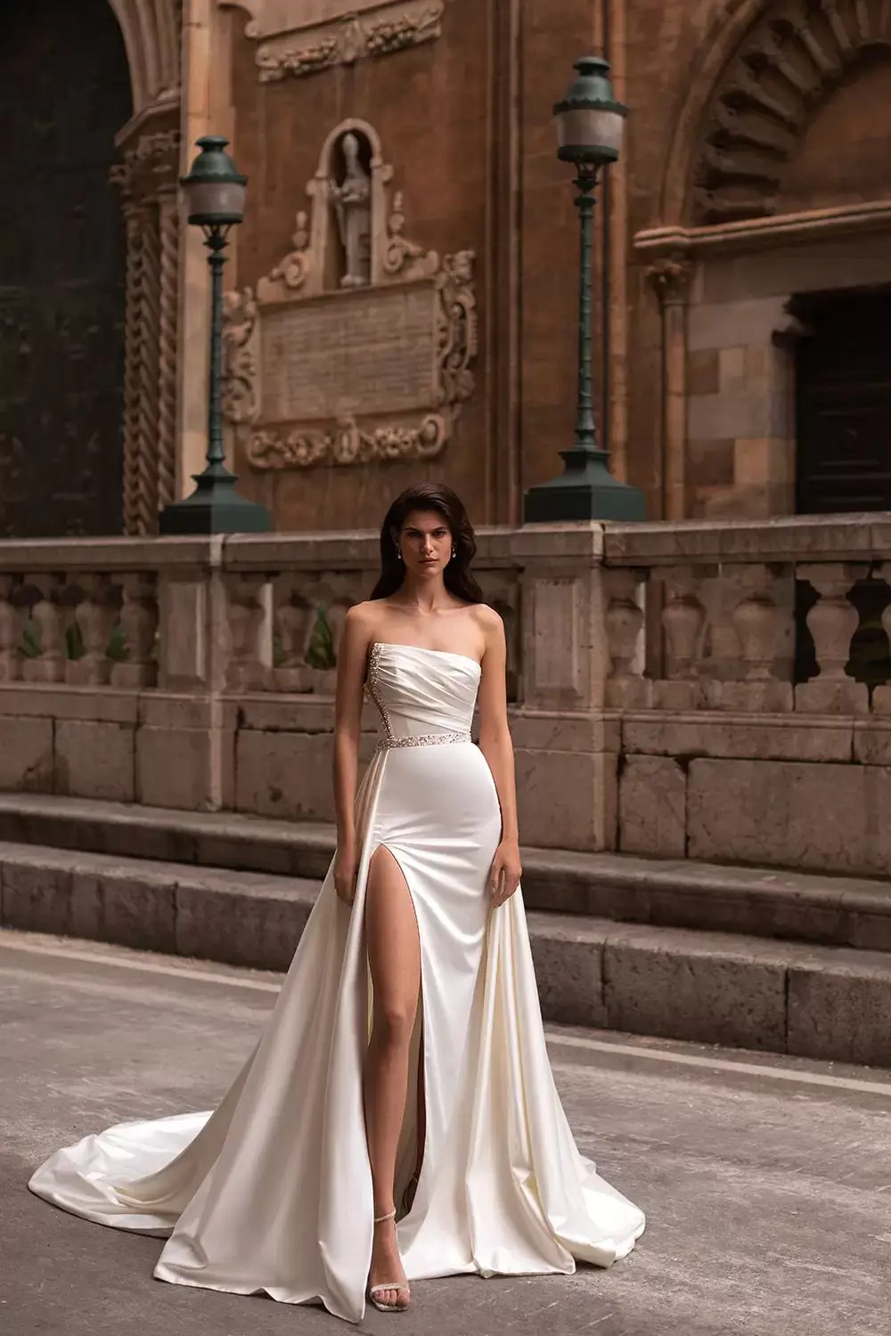Model is wearing a strapless satin wedding dress with crystal accents by eva lendel